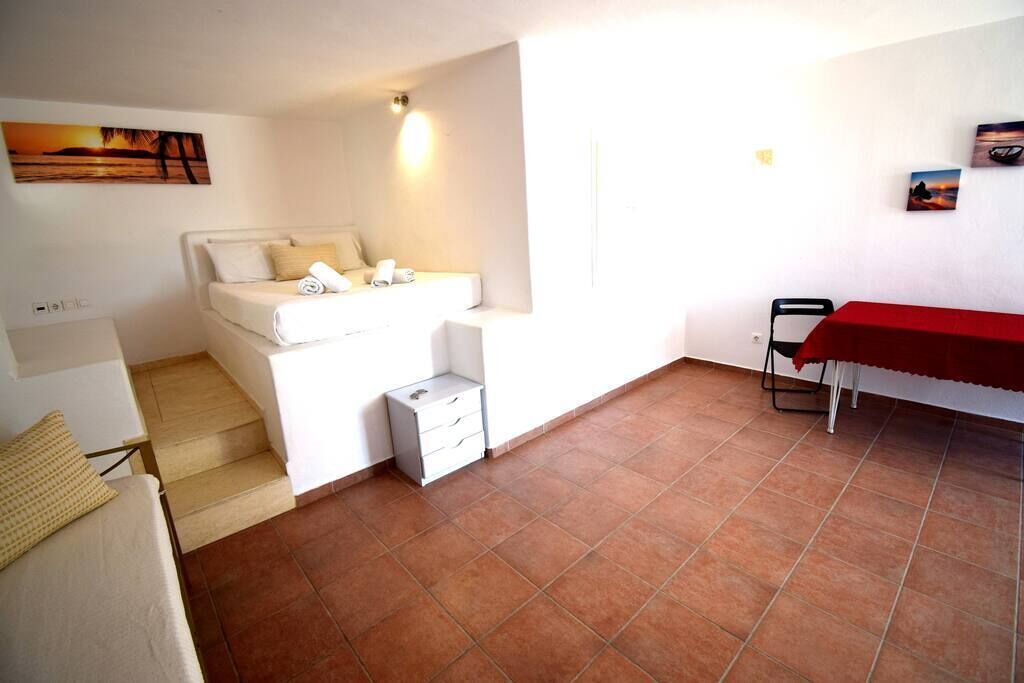Une pièce avec un lit, une petite table, une chaise et une nappe rouge.