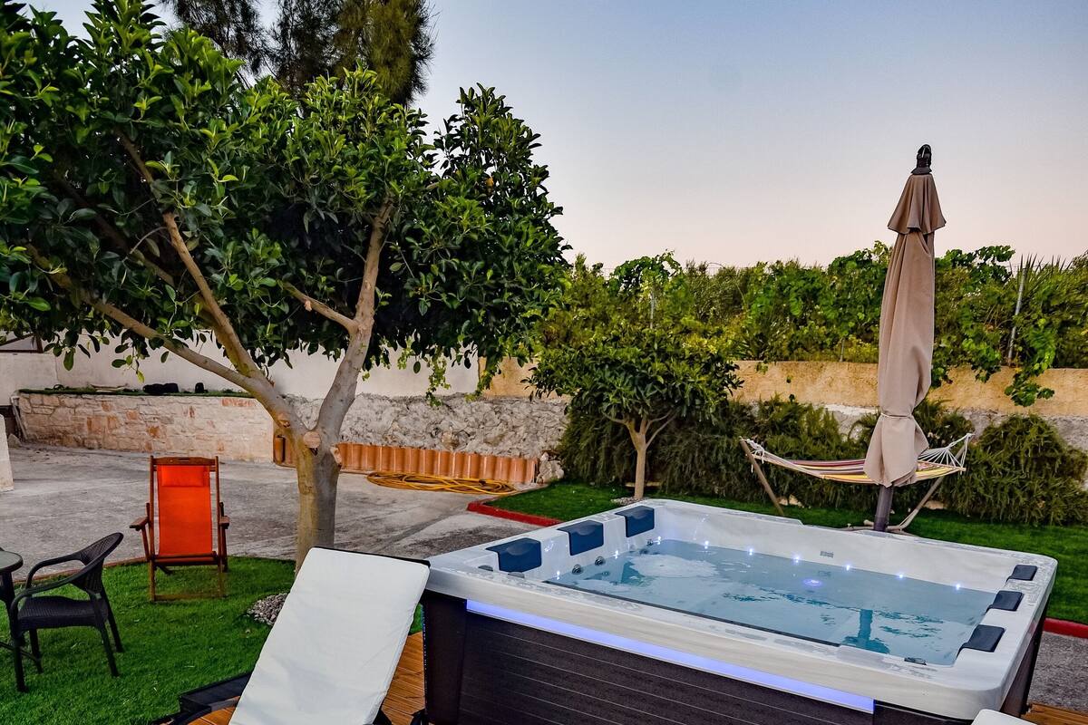 A wooden deck with two lounge chairs, a hot tub, and a small table.