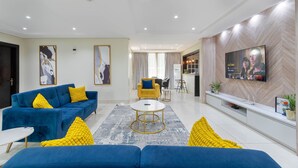 Uma sala de estar moderna com um sofá azul, uma mesa de centro redonda e uma TV de tela plana fixada na parede.
