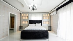 Ein modernes Schlafzimmer mit einem großen Bett, einer schwarzen Polsterbank, Einbauleuchten und einem Kronleuchter.