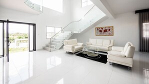 Ein geräumiges Wohnzimmer mit einer weißen Sofagarnitur, einem Glastisch und einer Treppe mit Glastrennwand.