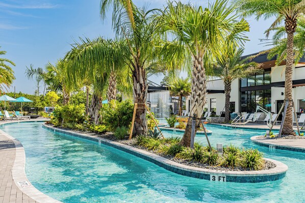 Una piscina con palmeras, sillas de descanso y un edificio con grandes ventanales.