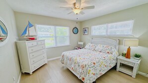 Ein Schlafzimmer mit Bett, Schminktisch, Nachttisch und Deckenventilator.