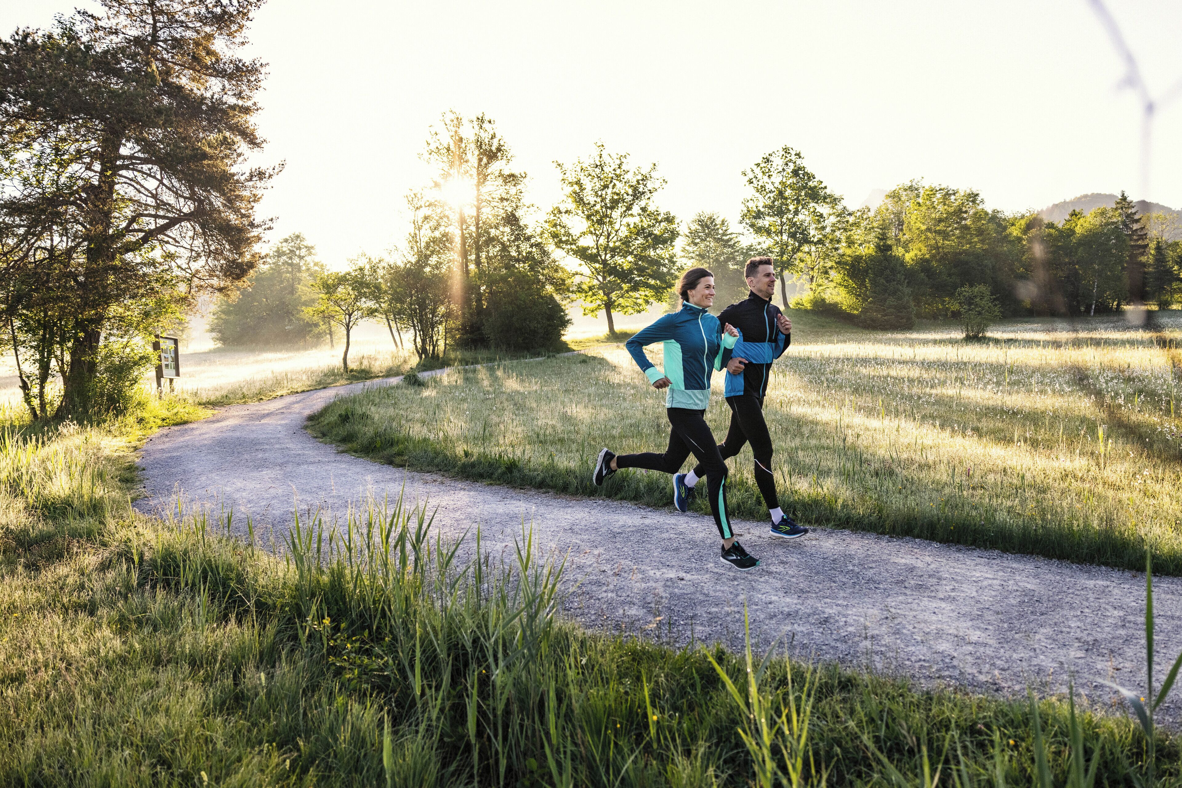 Two people jogging on a gravel path surrounded by grass and trees.