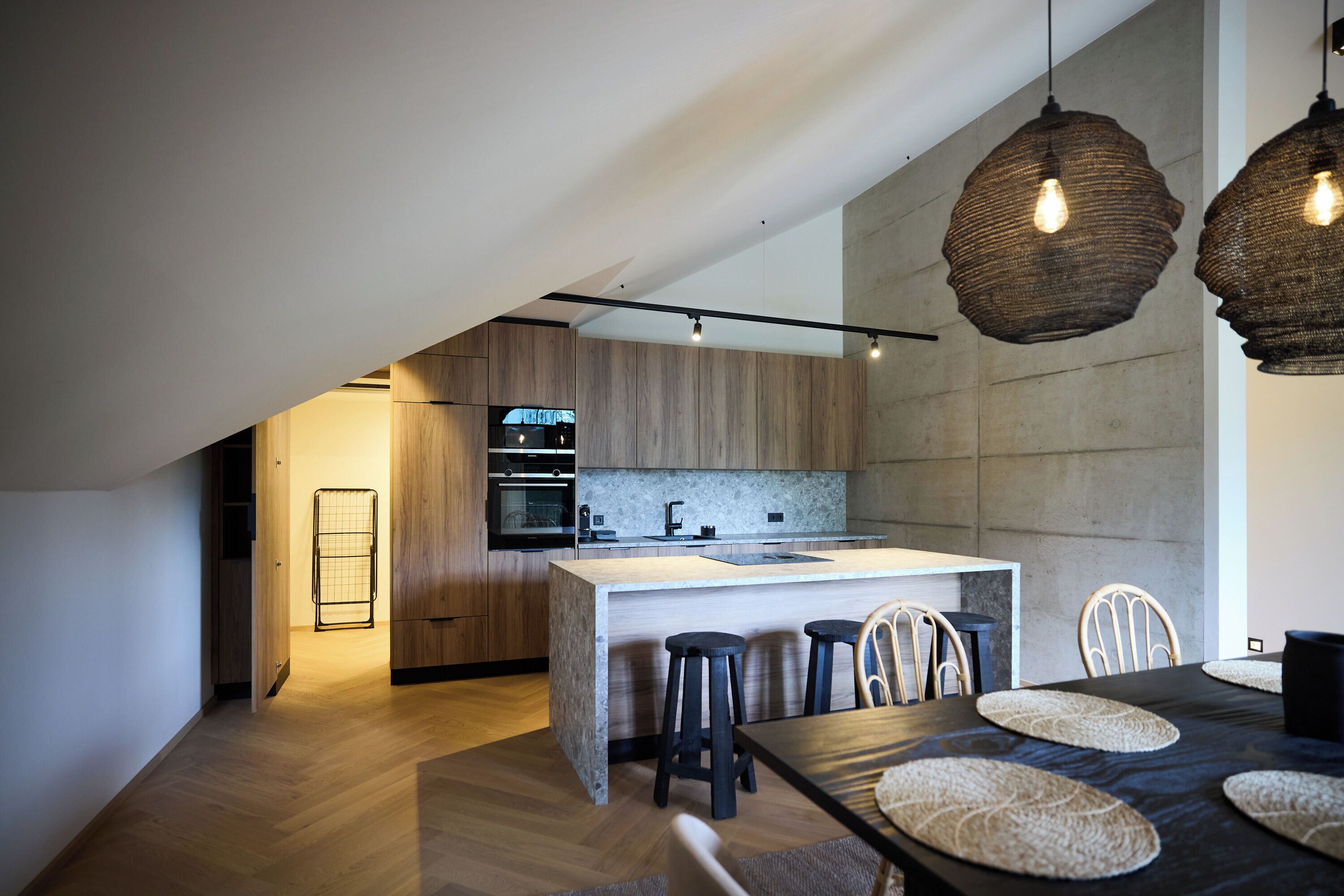 A modern kitchen with wooden cabinets, a central island with stools, and pendant lighting.