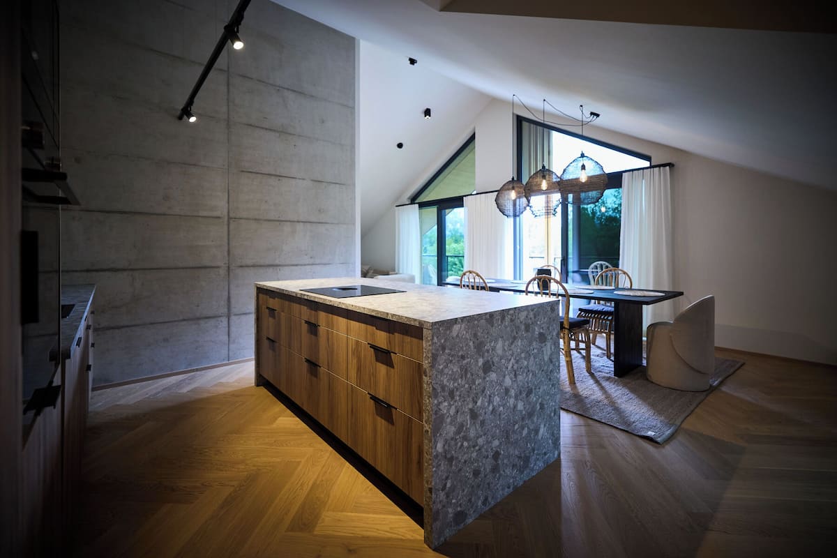 A modern kitchen with a large island, wooden cabinets, and a dining area with a table and chairs.