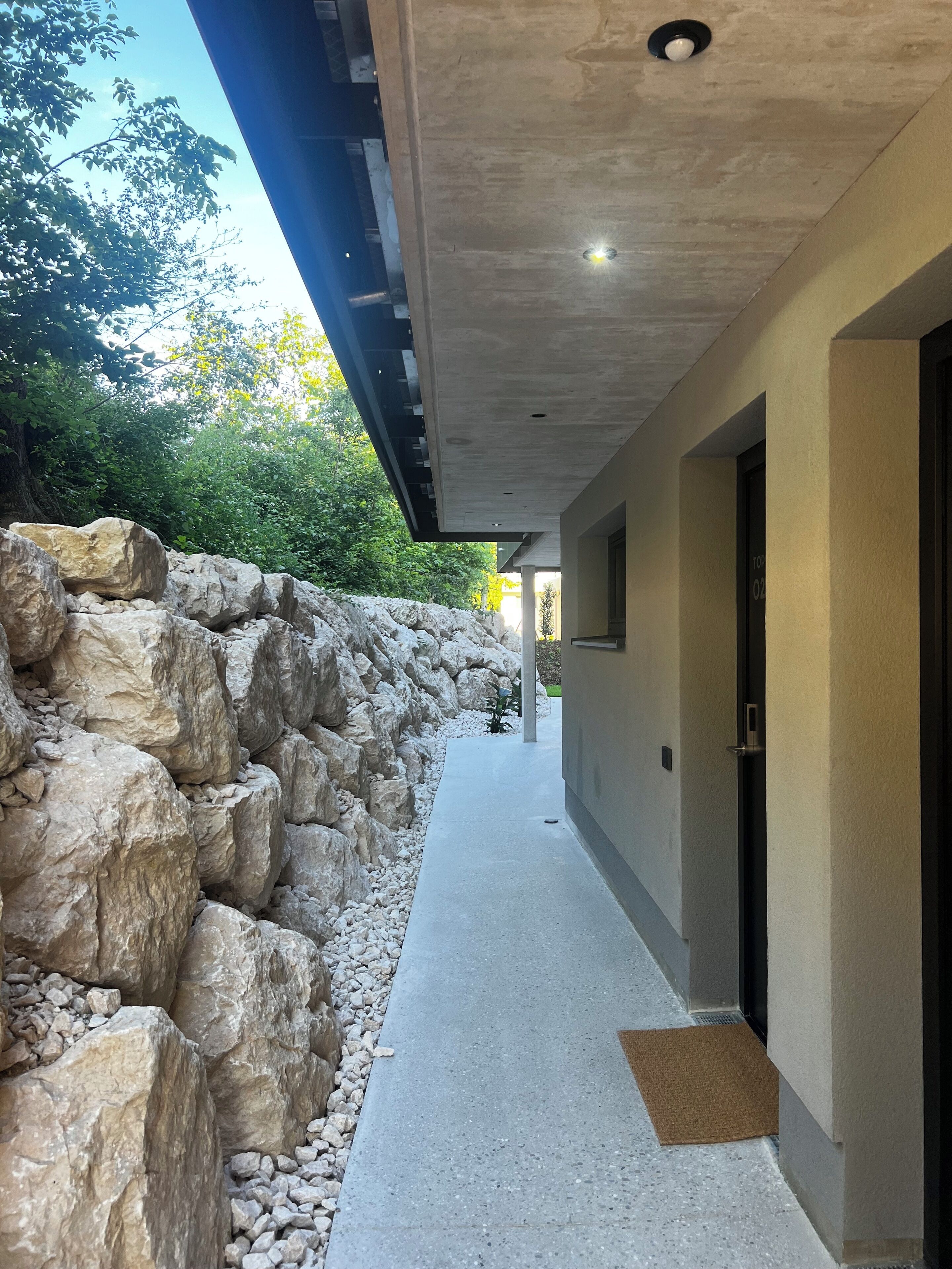 A modern building with a concrete exterior, a stone retaining wall, and a pathway leading to the entrance.