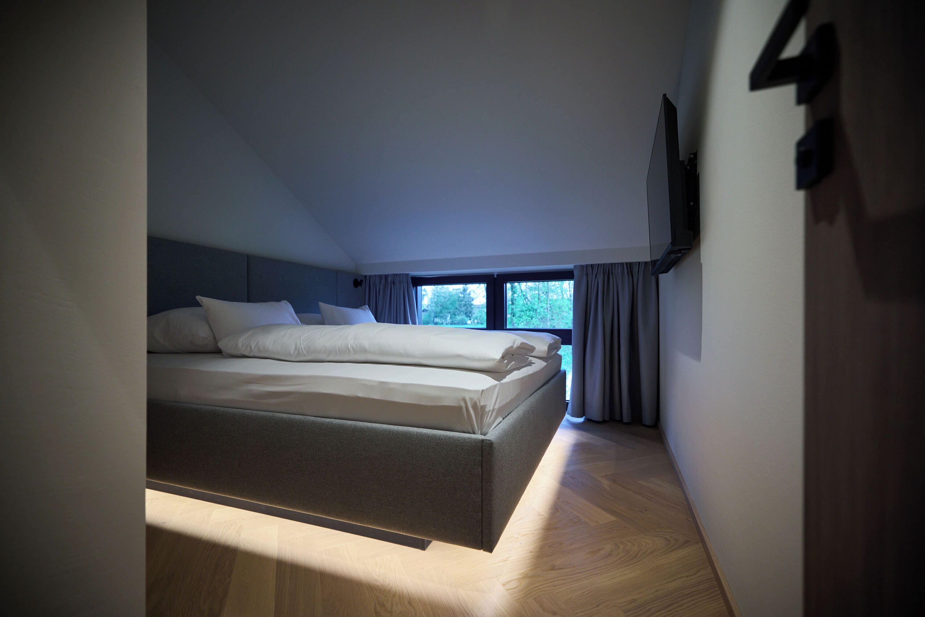 A modern bedroom with a bed, a TV mounted on the wall, and a window with curtains.