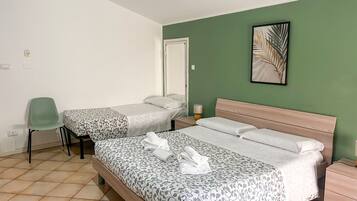 A hotel room with two beds, a chair, a nightstand with a lamp, and a framed picture on the wall.