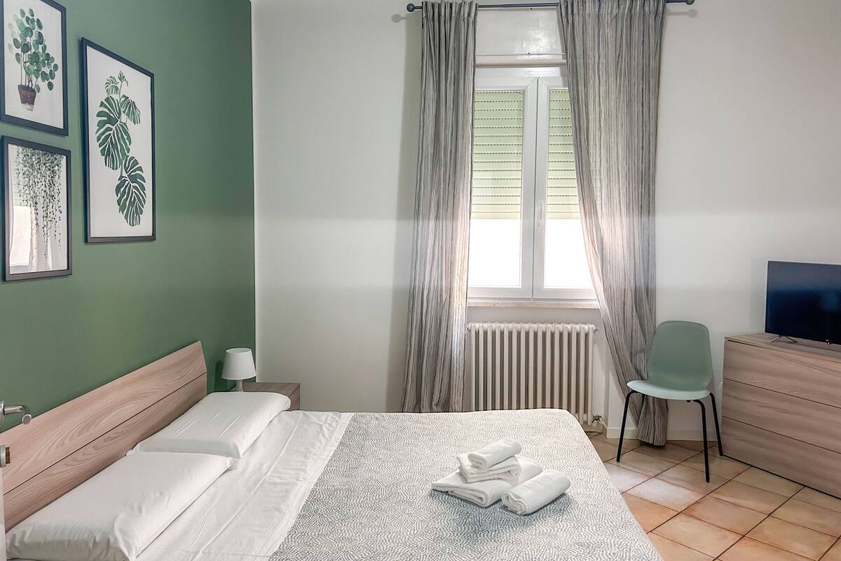 A neatly arranged bedroom with a bed, a chair, a TV, and a window with curtains.