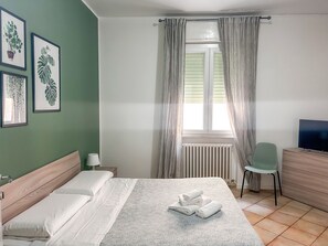 A neatly arranged bedroom with a bed, a chair, a TV, and a window with curtains.