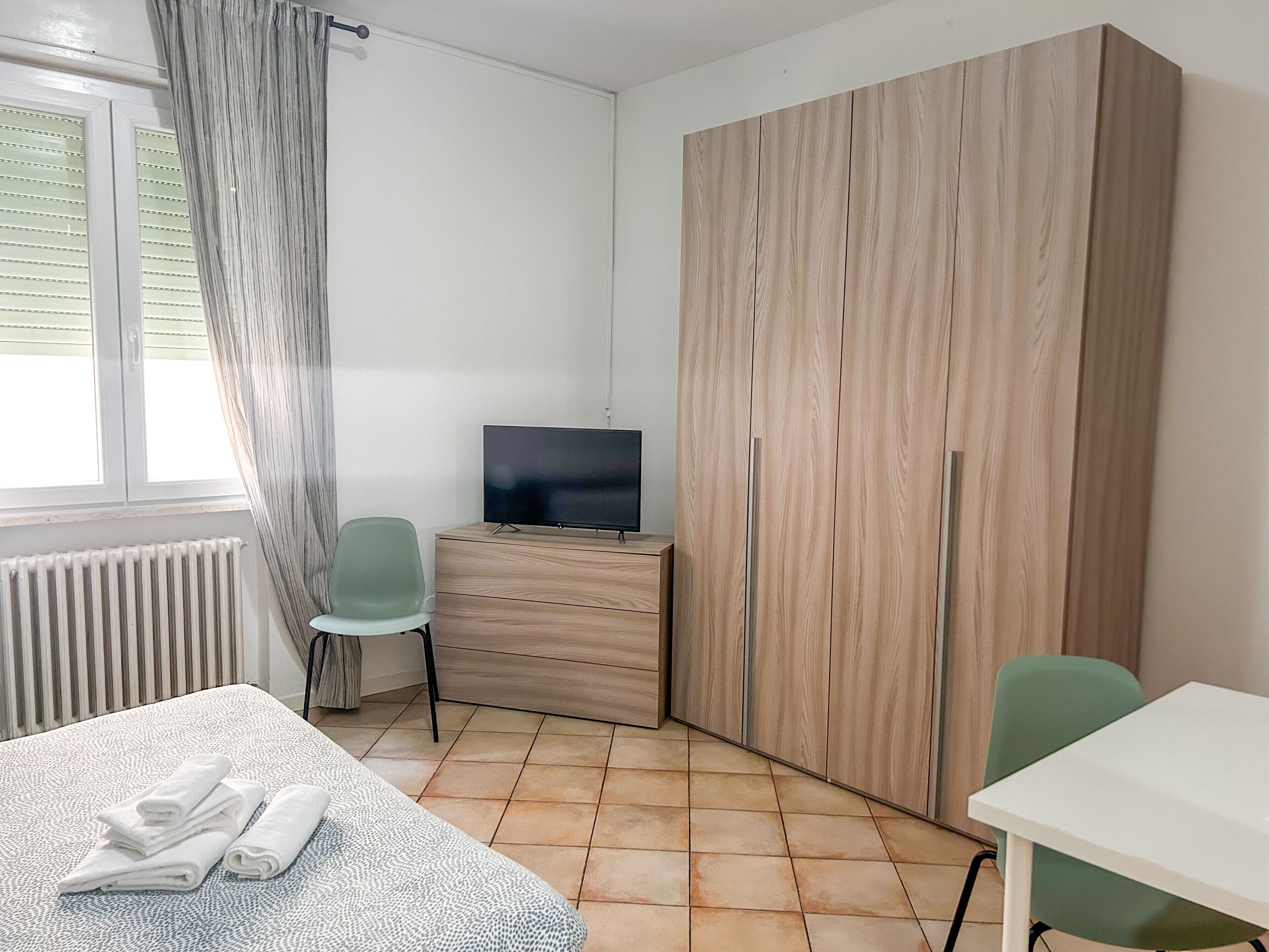 A room with a bed, a TV on a dresser, a chair, and a wardrobe.