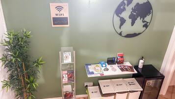 Et værelse med grøn væg, et verdenskort, et WiFi-symbol, en opslagstavle, en plante og skraldespande.