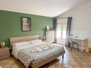 A bedroom with a bed, a desk, a chair, a radiator, and a window with curtains.