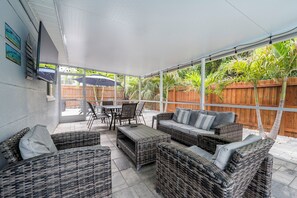 Une terrasse couverte, aménagée avec des meubles en osier, une table et des chaises.