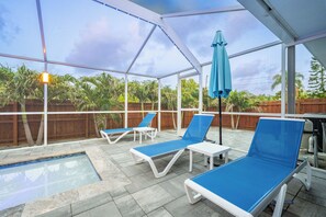 A covered outdoor area with a pool, lounge chairs, and a wooden fence.