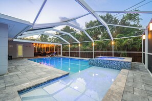 A covered swimming pool with a glass ceiling, surrounded by stone tiles and a wooden deck.
