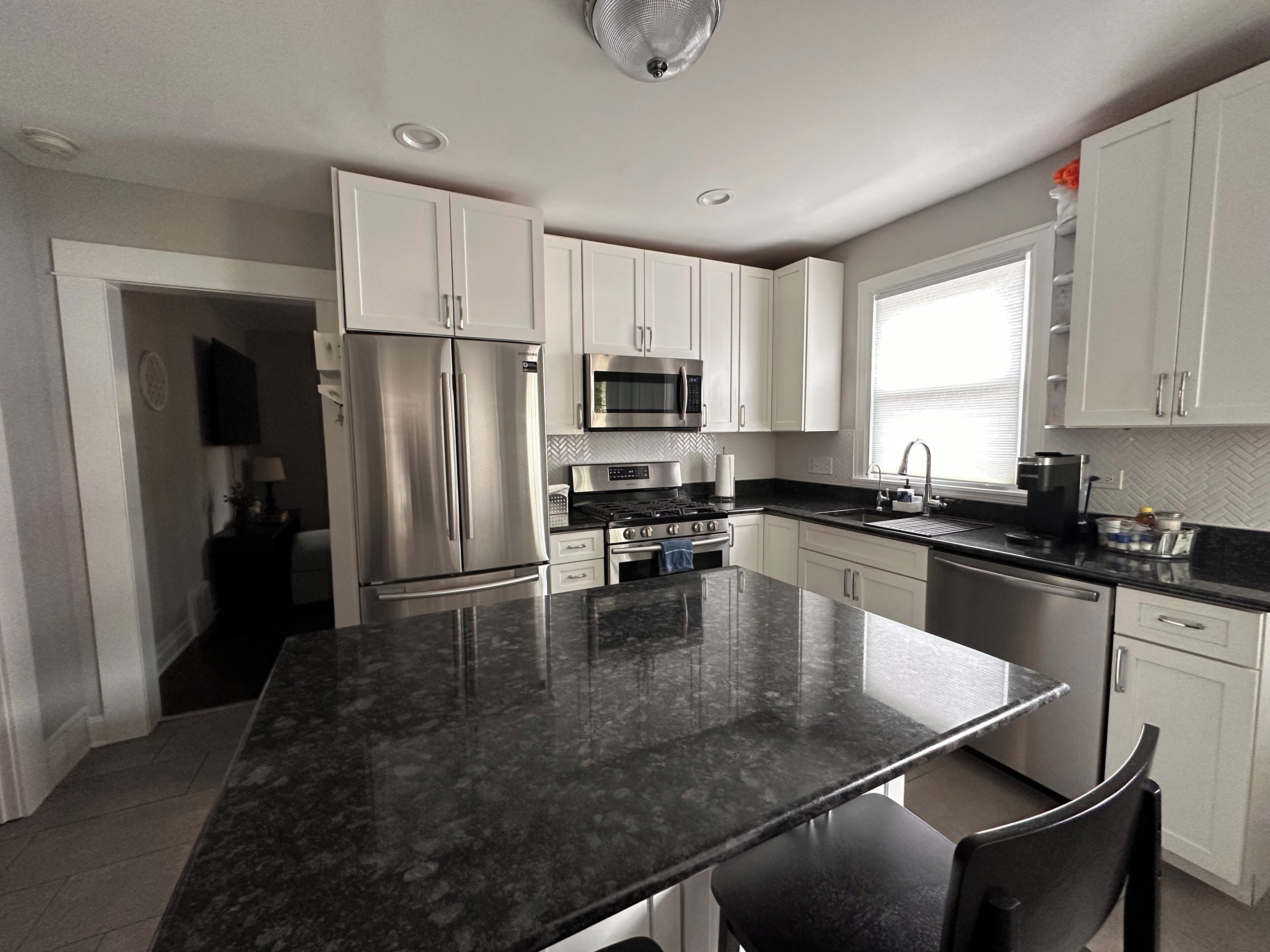 A modern kitchen with stainless steel appliances, a marble countertop, and white cabinetry.