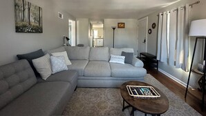 A living room with a grey sectional sofa, a coffee table with a tray, and a painting on the wall. - Cozy apartment right in Downtown Downers Grove (Downers Grove)