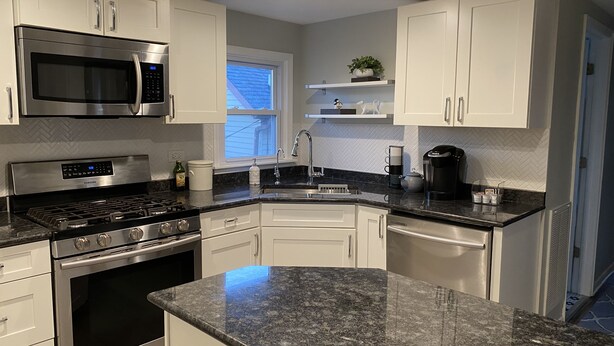 A modern kitchen with white cabinets, stainless steel appliances, granite countertops, and a window providing natural light. - Cozy apartment right in Downtown Downers Grove (Downers Grove)