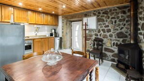 Una cuina amb armaris de fusta, una paret de pedra, una placa de cuina i una taula de menjador amb caires.