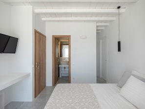 A bedroom with a bed, a TV mounted on the wall, and a door leading to a bathroom.