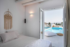 A bedroom with a bed, a macrame wall hanging, and a view of a swimming pool through an open door.
