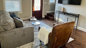 Un salon comprenant un canapé, un fauteuil, une table basse et un téléviseur fixé au mur.