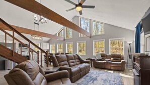 Ein geräumiges Wohnzimmer mit Ledersofas, einem großen Teppich und einem Deckenventilator.