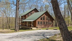 Eine zweistöckige Blockhütte mit grüner Dachdeckung, umgeben von Bäumen.