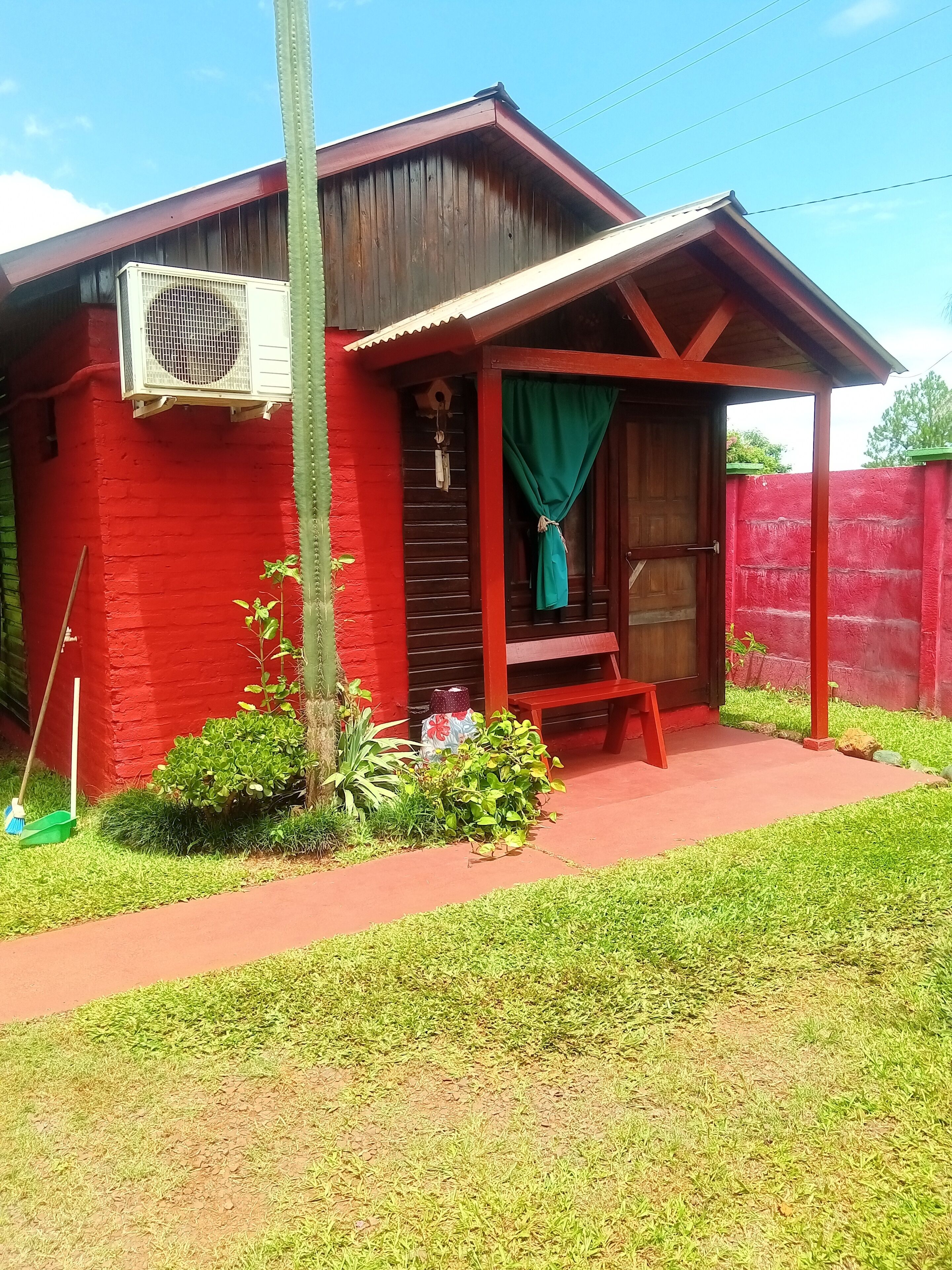 A red building with a covered porch, a small garden, and a green curtain.
