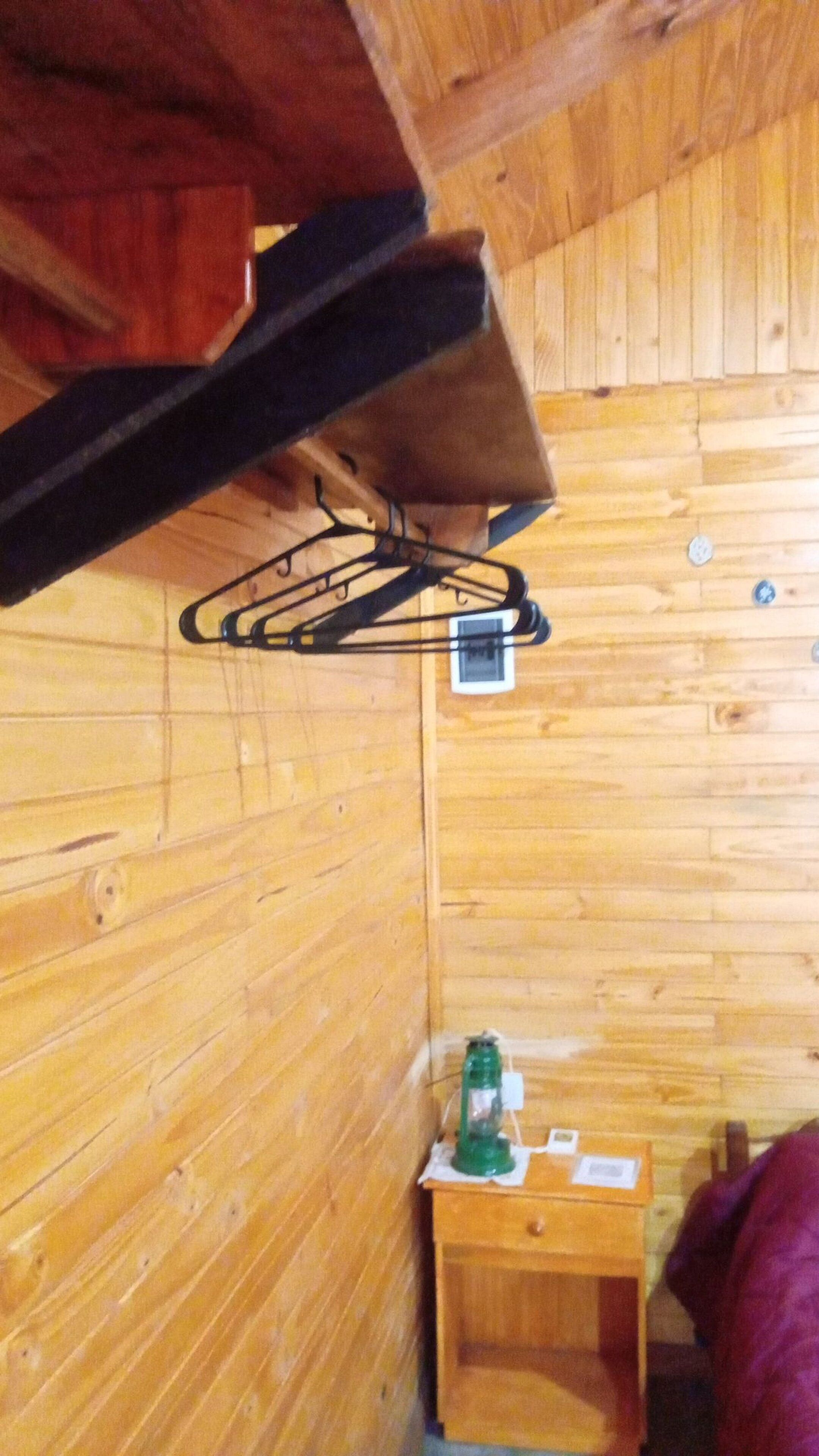 A wooden cabin interior with a bed, a small wooden table, and a wall-mounted shelf.