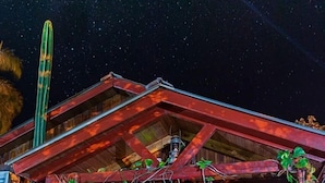 A rustic wooden building with a porch, a large cactus, and a starry night sky. - Bungalows El Pindó (Colonia Alberdi)