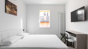 Hotellihuone, jossa on suuri sänky, työpöytä, tuoli, televisio ja ikkuna, josta on näkymä rakennuksiin.