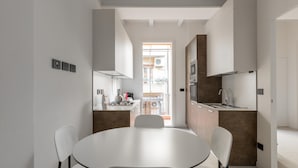 A modern kitchen with white cabinets, a central island, and a dining area with a round table and chairs. - White Daisy Apartment by Wonderful Italy (Bologna)