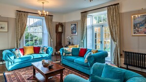 A spacious living room with a blue sofa set, a wooden coffee table, and a large window with curtains.