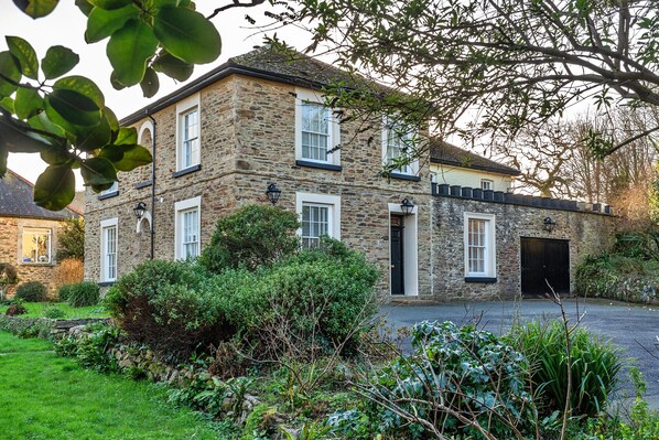 A stone building with multiple windows and a black door, surrounded by greenery. - The Old Counting House (Gweek)