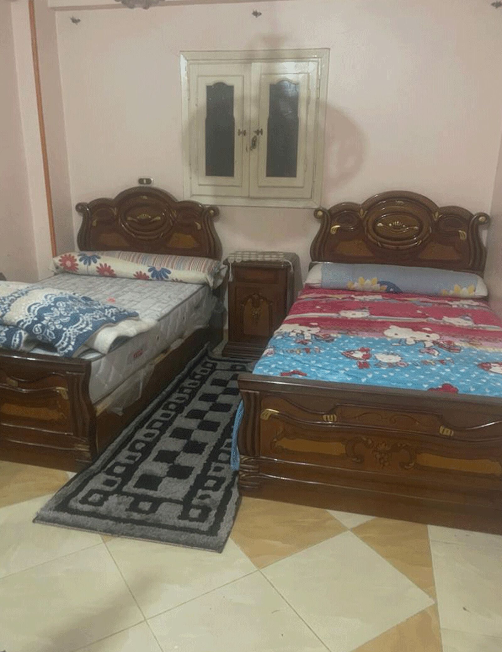 A bedroom with two wooden beds, a small wooden nightstand, a patterned rug, and a wall-mounted cabinet.