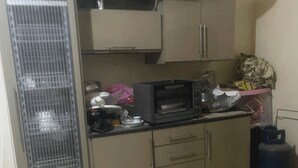 A compact kitchen with a microwave, a gas cylinder, and a small refrigerator.