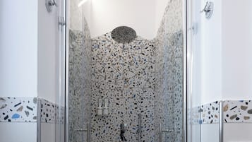 Una doccia con pareti in vetro, rivestimento in piastrelle screziate e pavimento bianco.