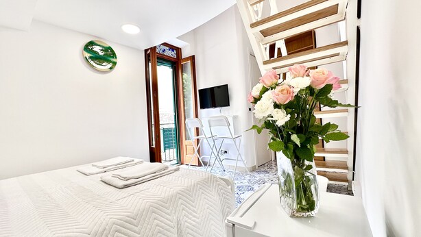 A hotel room with a bed, a desk, a chair, a TV, and a vase with flowers. - Residenza Giuseppe (Amalfi)