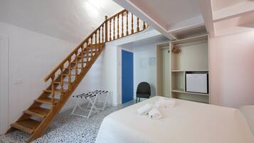 A bedroom with a wooden staircase, a bed with white linens, a small table, and a chair.