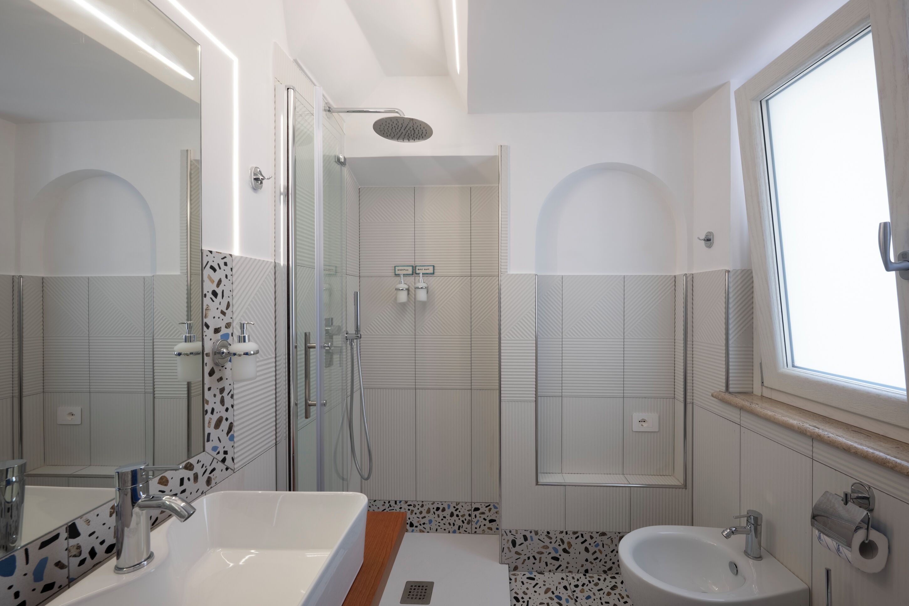 Une salle de bain moderne dotée d’une douche à parois de verre, d’un grand miroir et d’un meuble-lavabo avec un évier et un plan de travail.