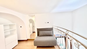 A small, bright room with a grey sofa, a white wardrobe, and a balcony with a metal railing. - Residenza Giuseppe (Amalfi)