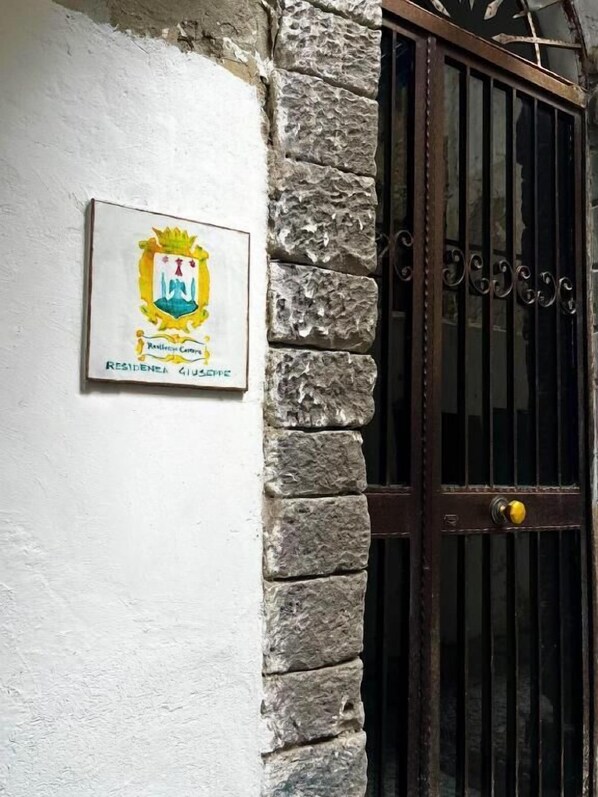 A stone wall with a metal gate and a plaque with a coat of arms. - Residenza Giuseppe (Amalfi)