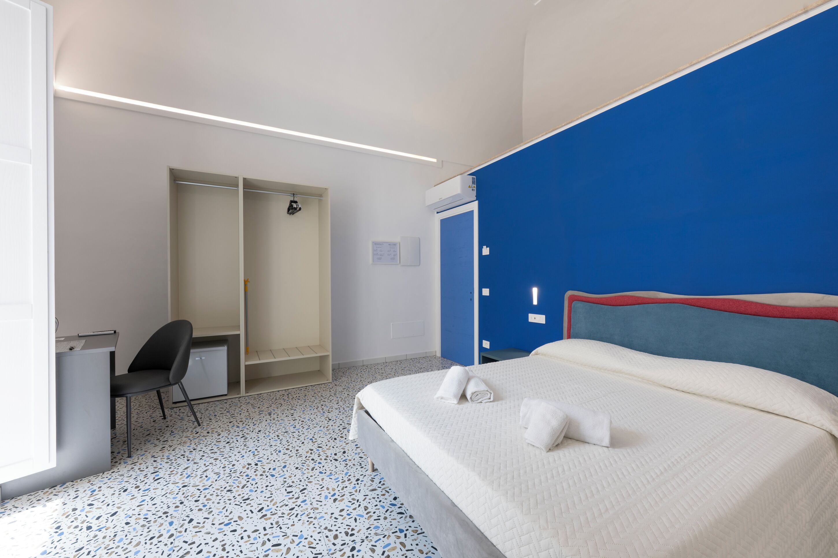 A hotel room with a bed, a desk, a chair, a wardrobe, and a bathroom.