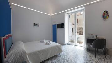 A bedroom with a bed, a desk, and a chair. There is a door leading to a balcony.