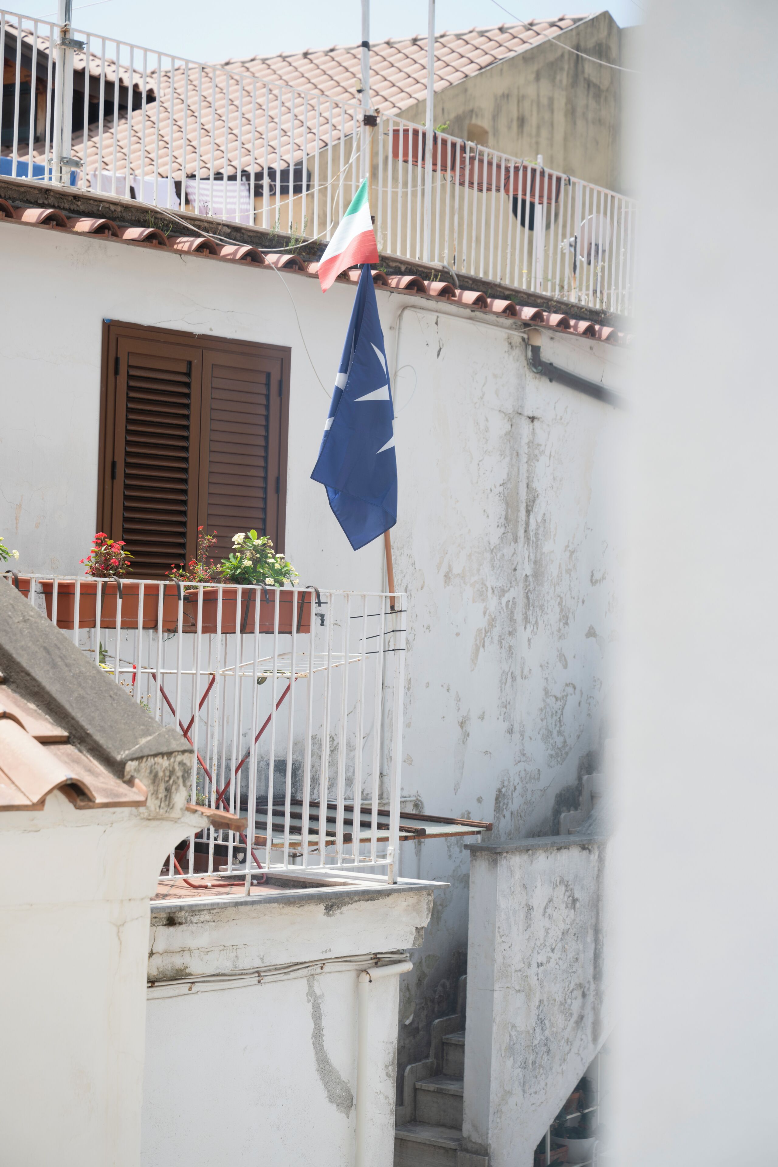 Un bâtiment doté d’un balcon, d’un drapeau et d’une fenêtre avec des volets.