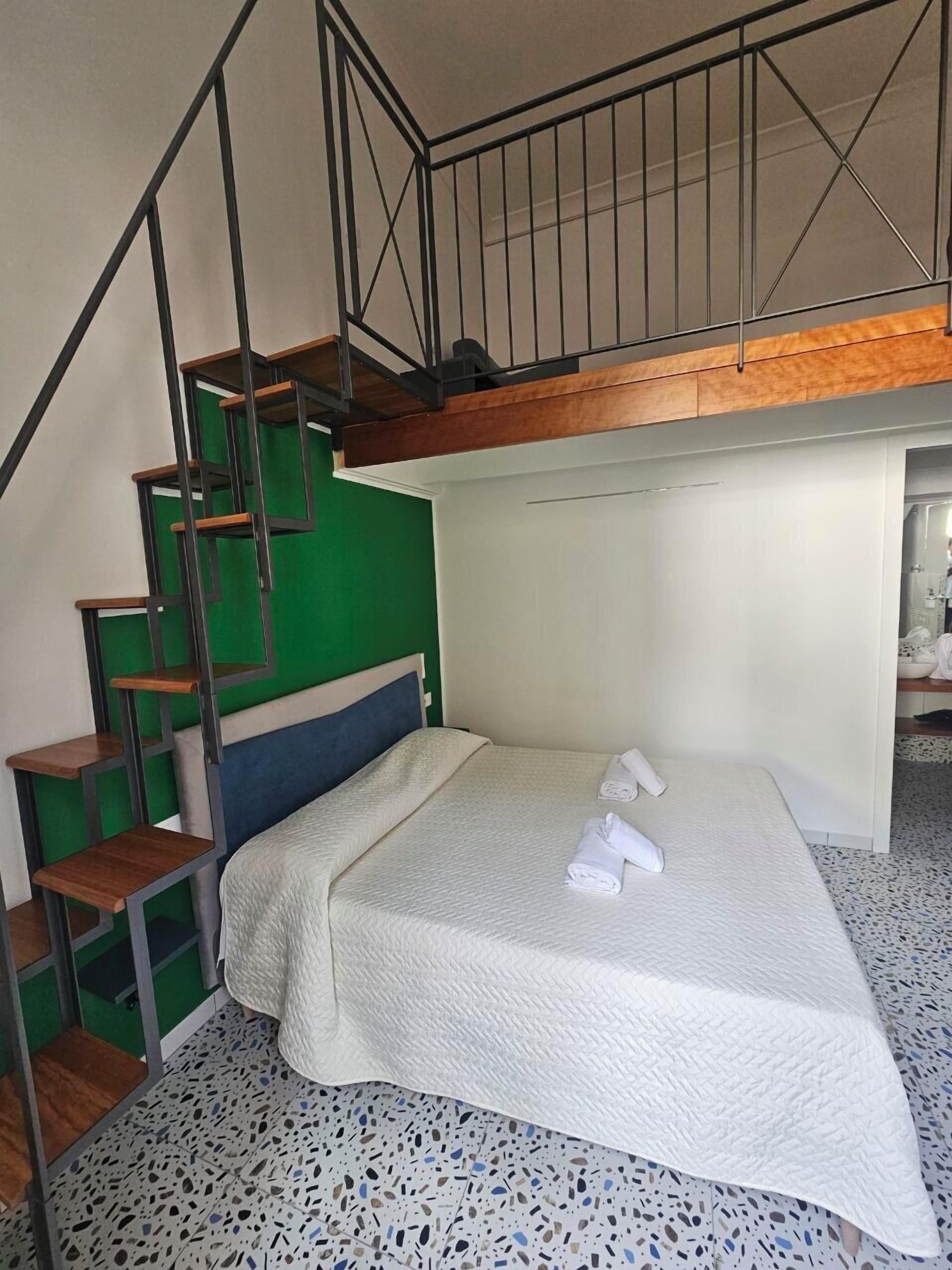 A compact room with a bunk bed, a staircase with a green wall, and a small wooden shelf.
