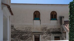 A balcony with a table and two chairs, a building with arched windows, and a tiled floor. - Residenza Giuseppe (Amalfi)